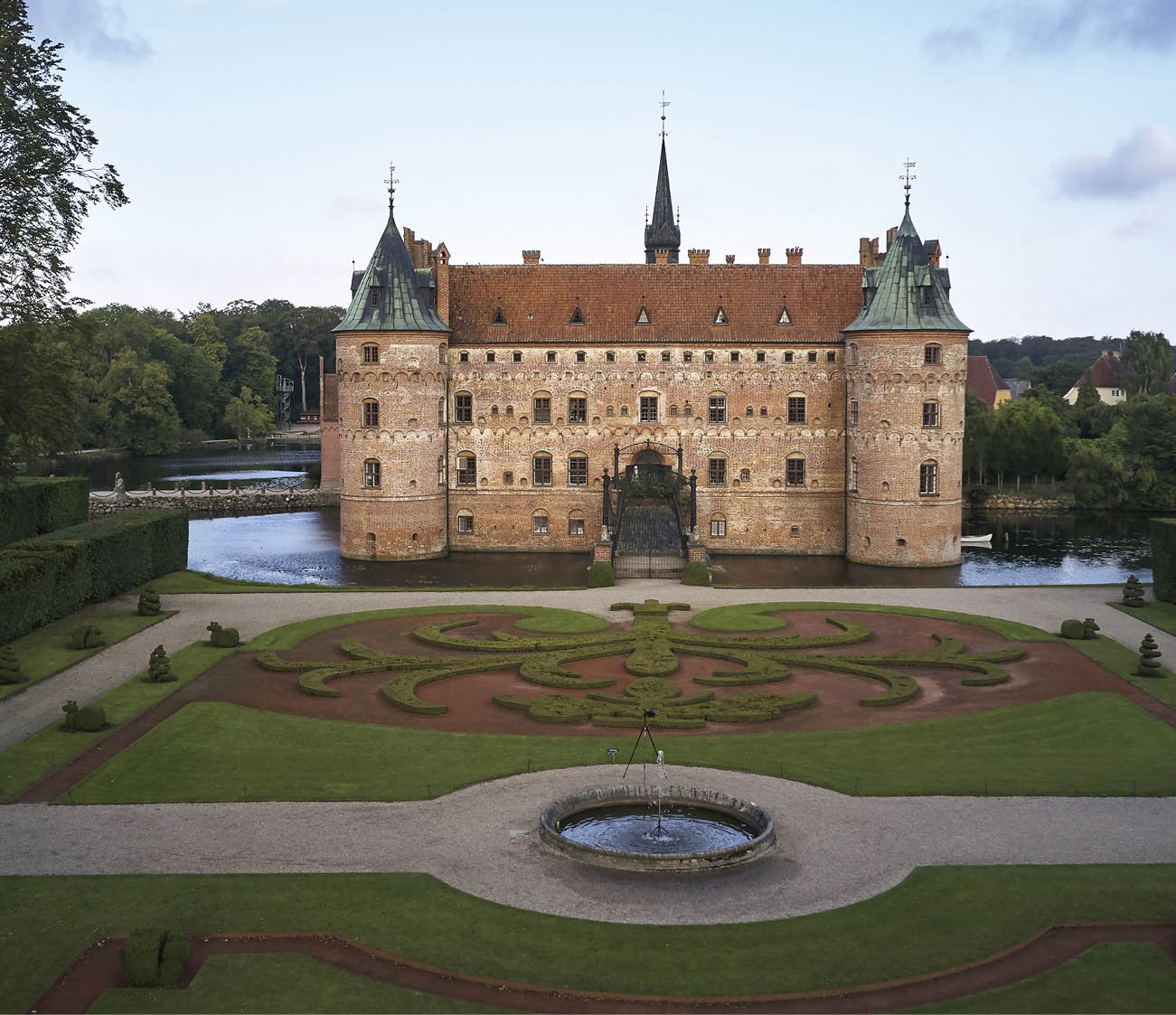 A large castle with a moat and a fountain in front of it. Description generated by AI